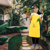 mood shot of girl wearing Daily Dump Compost Apron in outdoor garden and holding rake from gardening toolkit and potted plant in the other