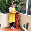 mood shot of girl wearing Daily Dump Compost Apron in outdoor garden and holding rake from gardening toolkit and potted plant in the other