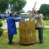 Daily Dump Bamboo leaf composter 32 inches diameter in use in community garden for composting dried leaves with 2 housekeeping staff pressing down to compress pile 