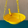 Yellow Bird feeder hanging 3 D against corrugated background