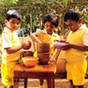 Young smiling boy seated outdoors reading and disposing banana peel into Daily Dump Nano khamba by his side.