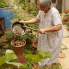 Pair of Daily Dump Prithvi Khambas home composters in outdoor garden with young girl adding kitchen waste to one. 
